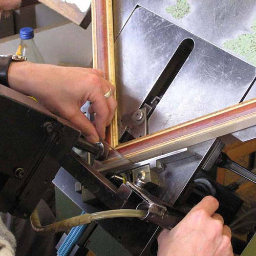 Hände halten einen Bilderrahmen und bedienen eine Maschine in einer Werkstatt